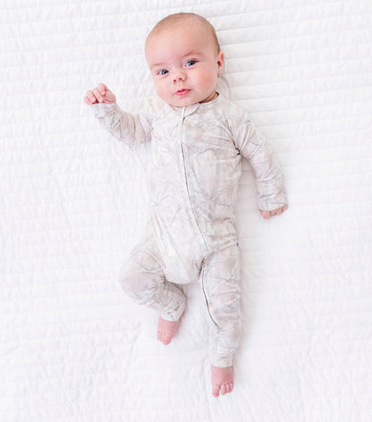 Baby in a tree camo onesie lying on a textured white blanket