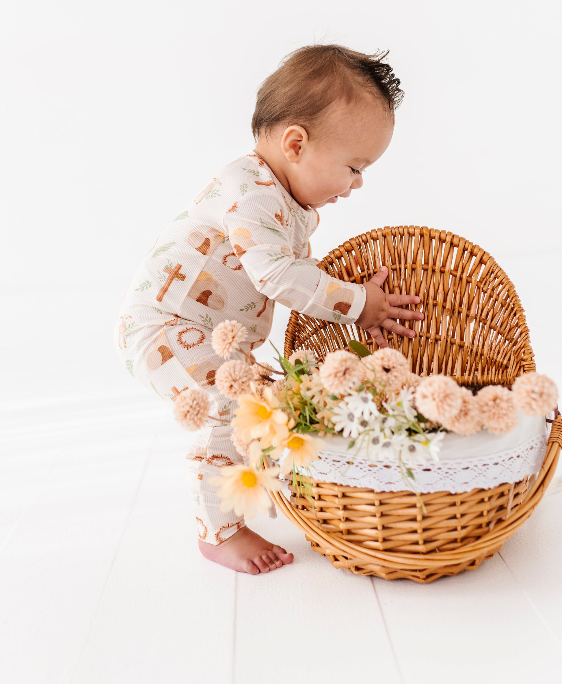 Baby playing with a wicker basket filled with flowers on a white background