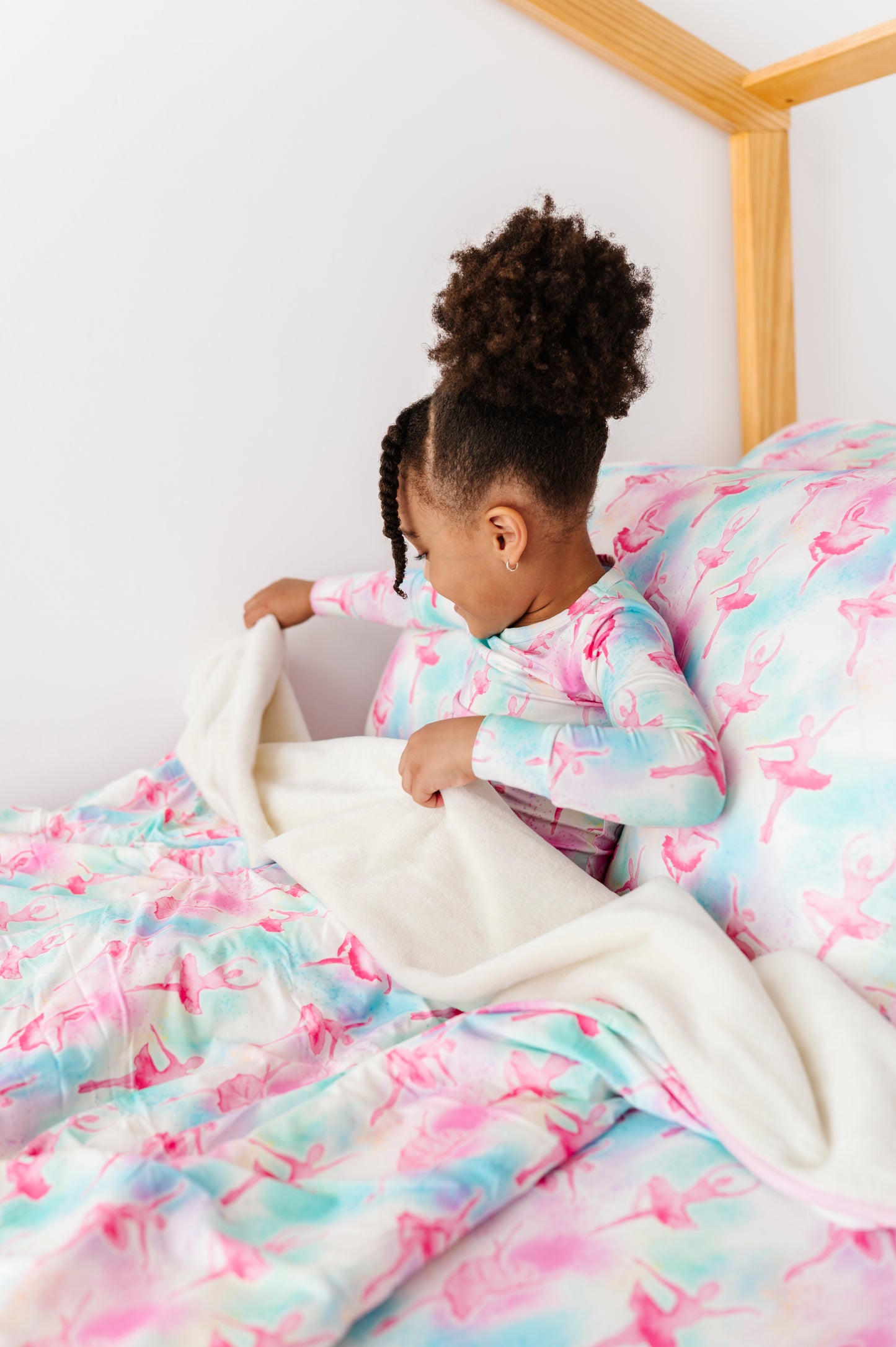Child in a colorful ballet-themed room, sitting on a bed with a ballerina plush blanket