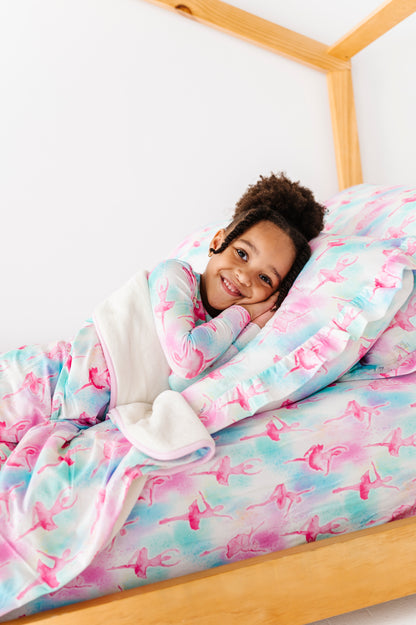 Child wrapped in a watercolor bamboo blanket with ballet pattern on a bed.