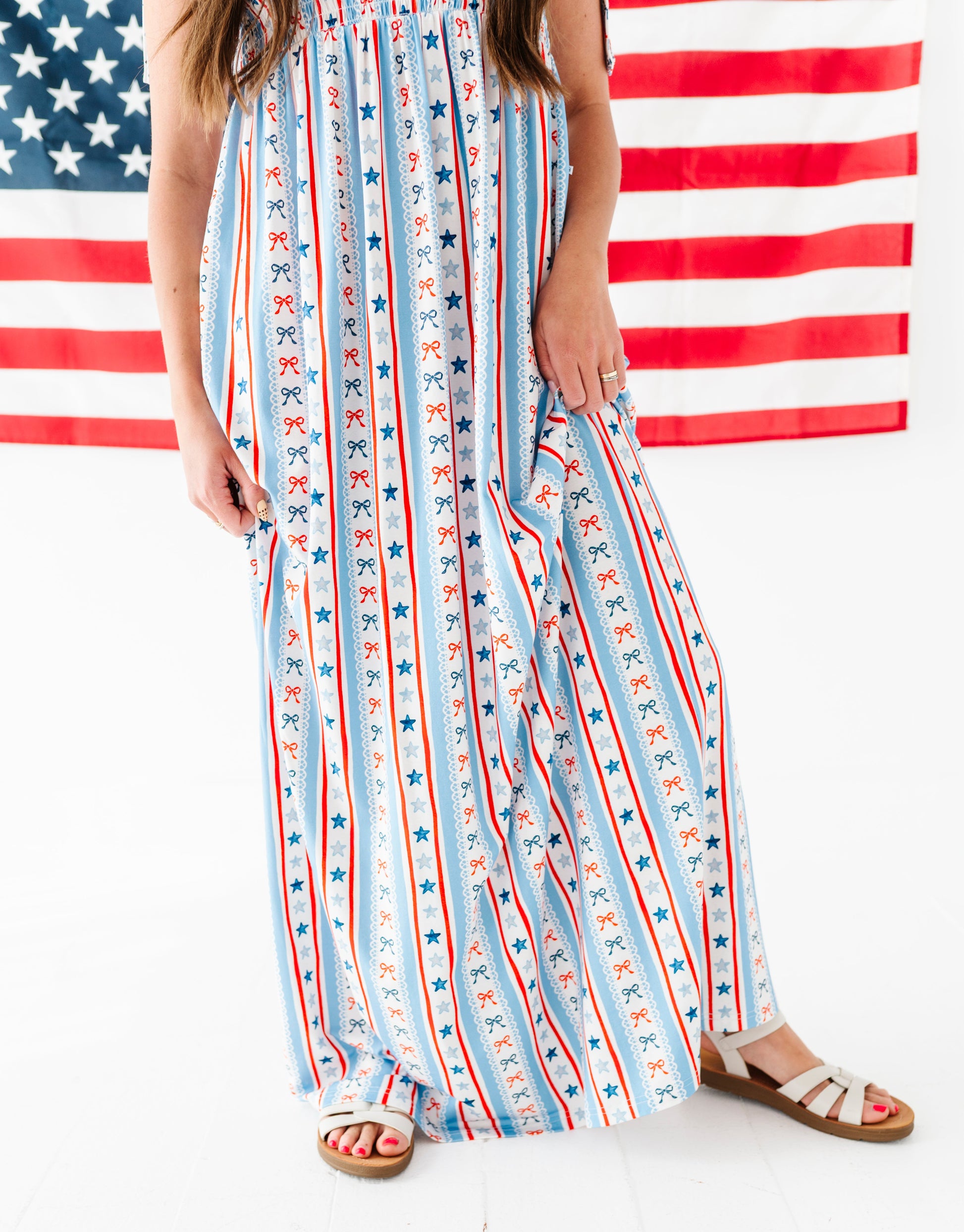Woman wearing a bamboo-cotton maxi dress with red, white, and blue stripes and stars in front of an American flag.
