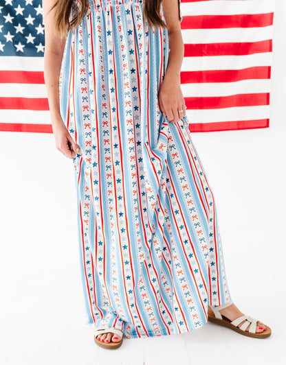 Woman wearing a bamboo-cotton maxi dress with red, white, and blue stripes and stars in front of an American flag.