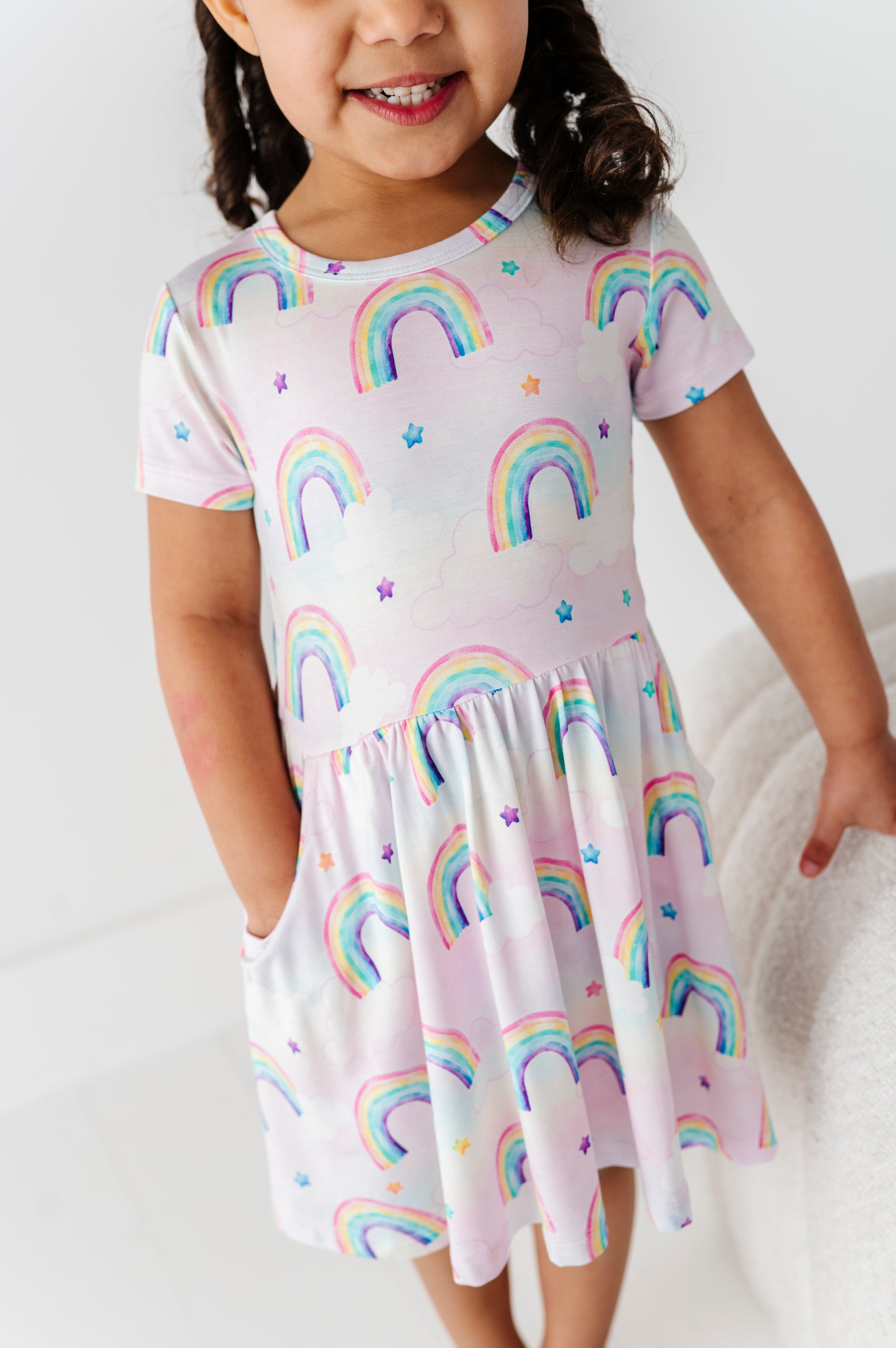 Child wearing a bamboo dress with watercolor rainbow patterns on a white background
