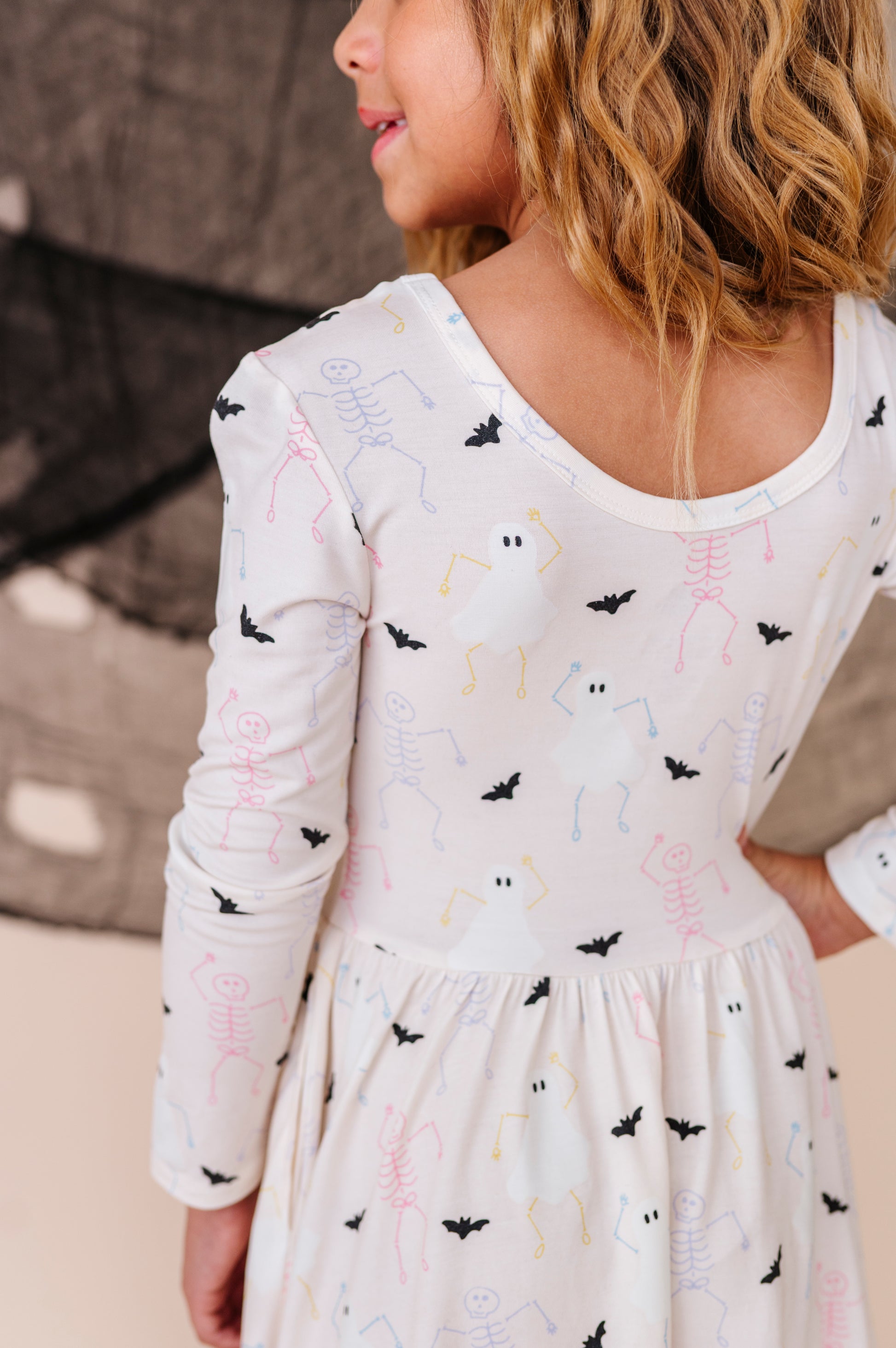 Child wearing a white dress with black bat pattern on a neutral background
