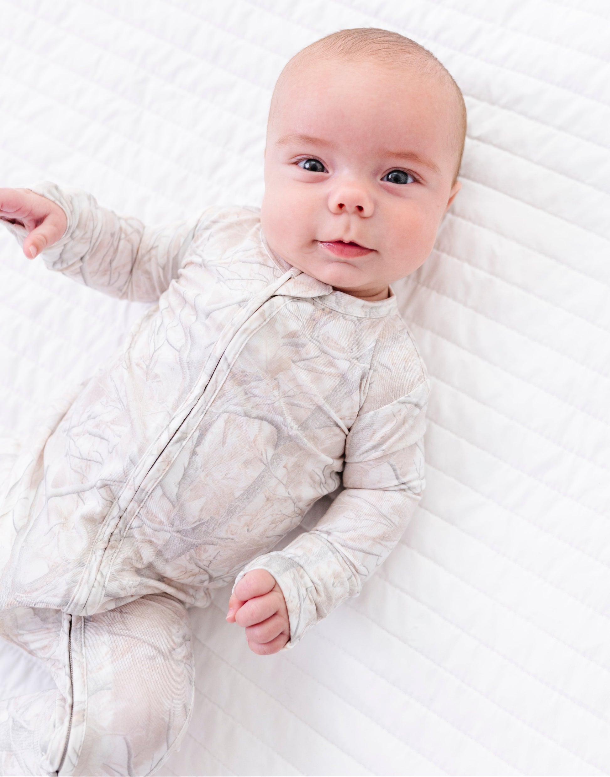 Baby in a tree camo romper lying on a white blanket