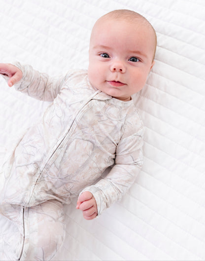 Baby in a tree camo romper lying on a white blanket
