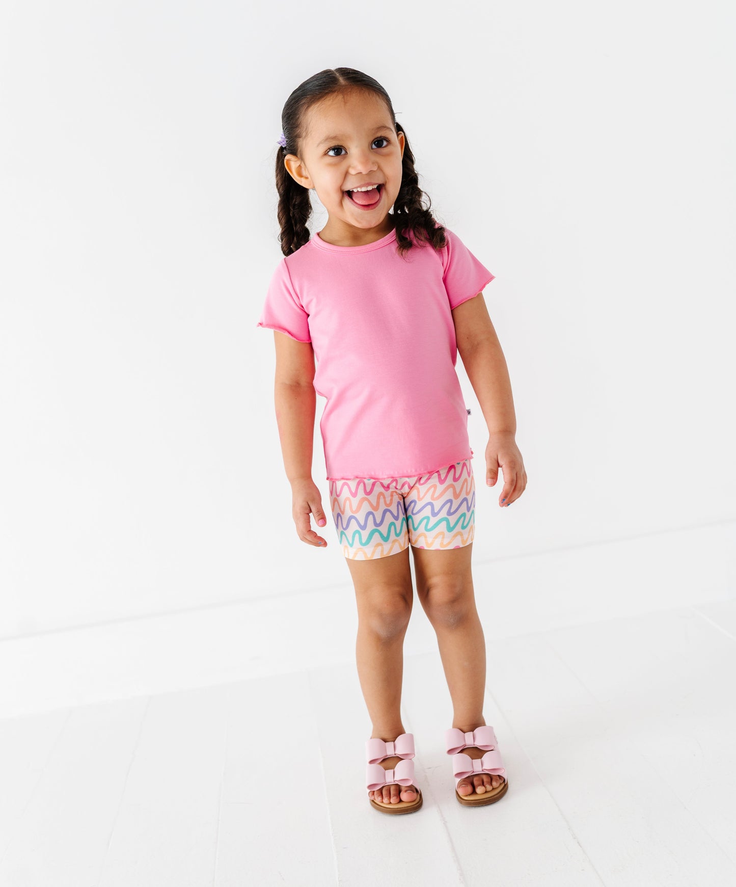 Young girl wearing a pink bamboo/cotton shirt and colorful bamboo biker shorts on a white background