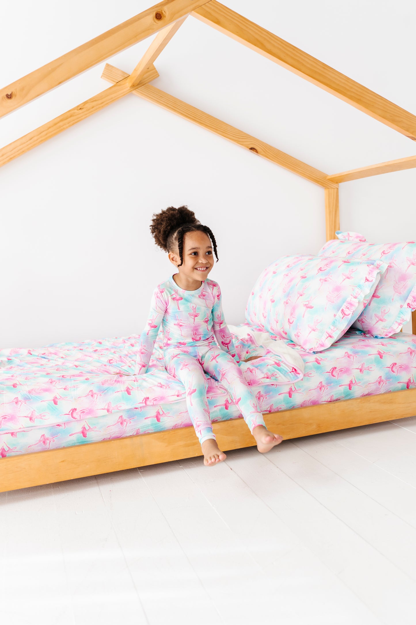 Child in bamboo pajamas sitting on a wooden bed with matching bamboo bedding 