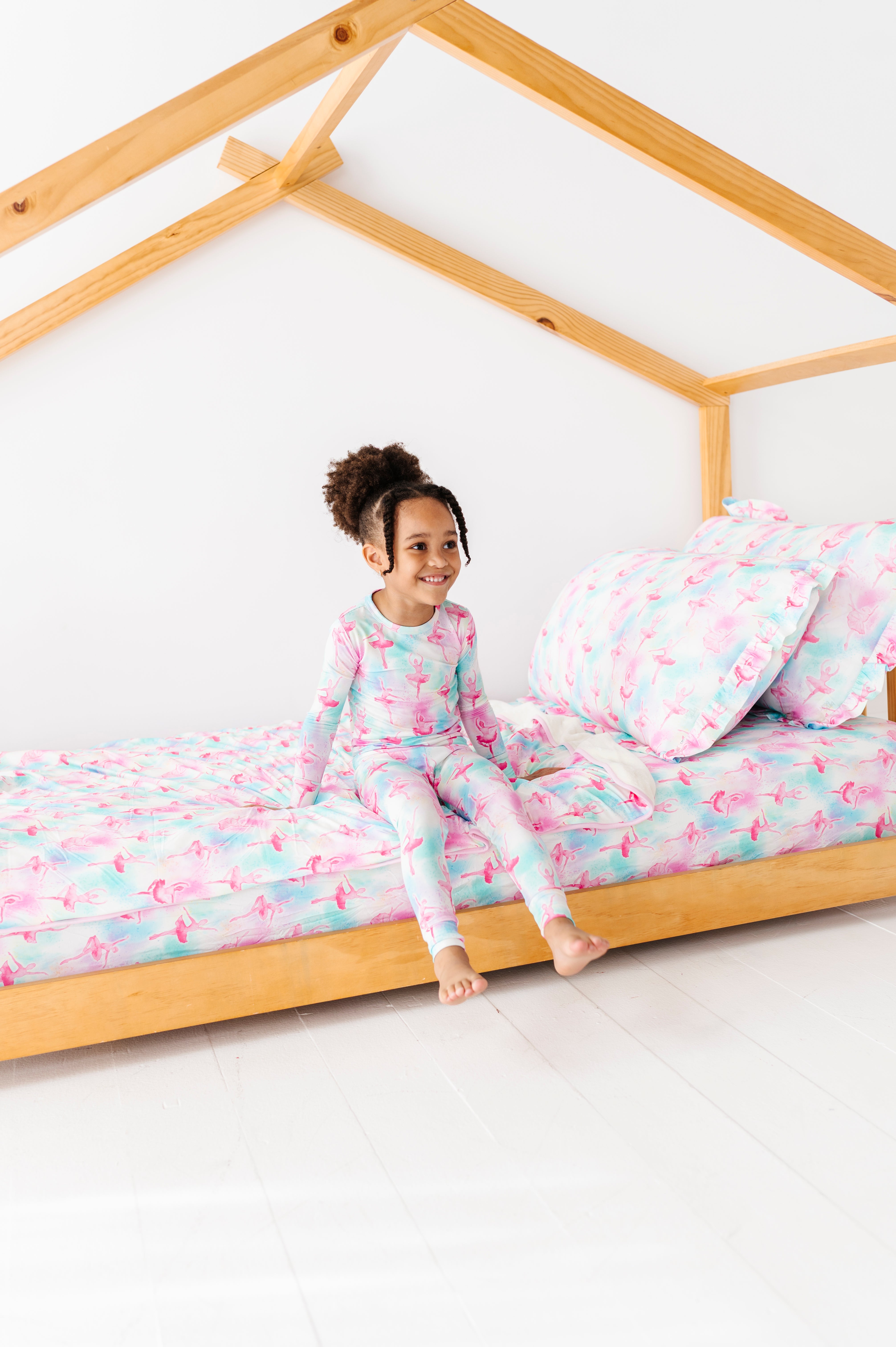Child in bamboo pajamas sitting on a wooden bed with matching bamboo bedding 
