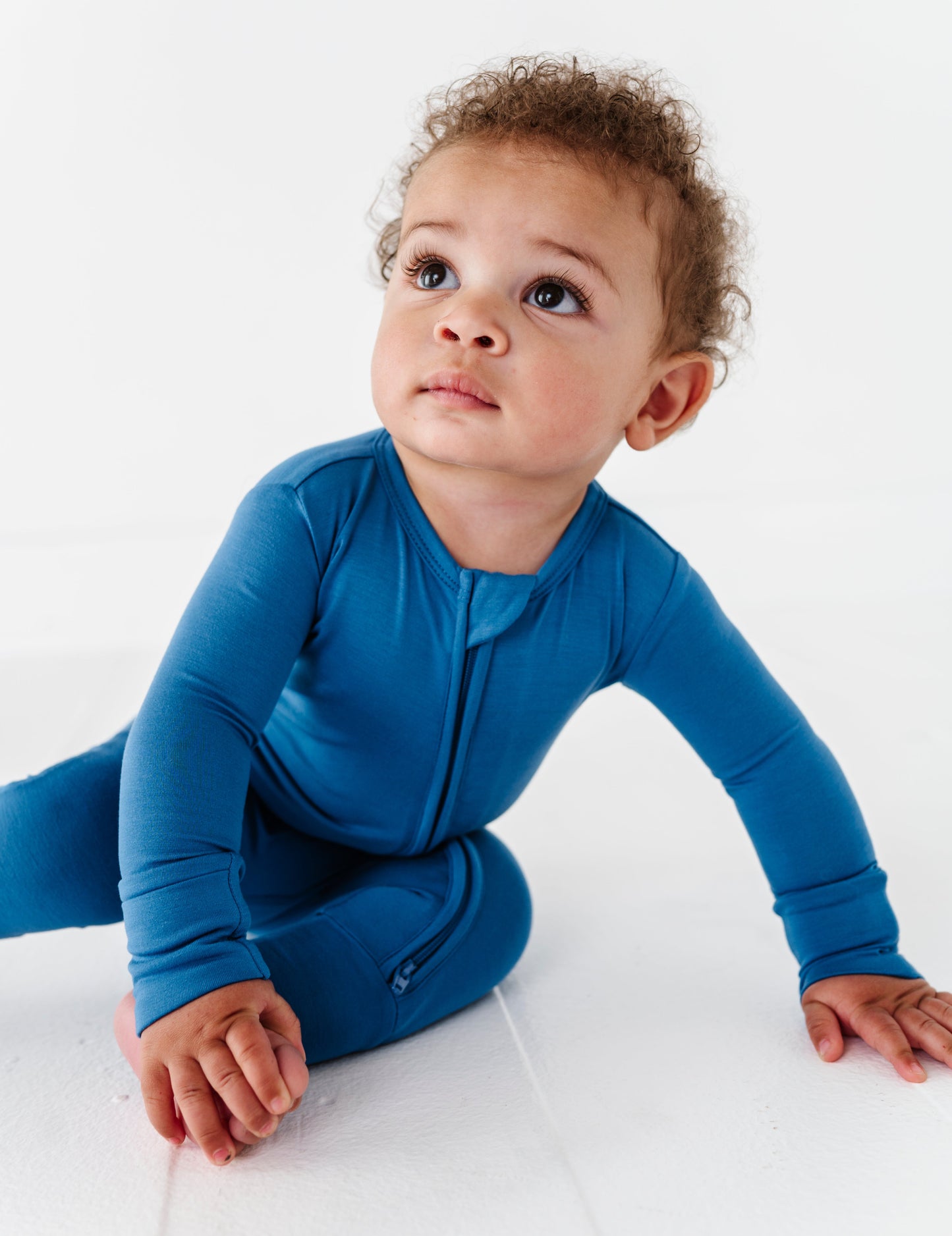 Baby in a blue bamboo convertible romper sitting on a white surface