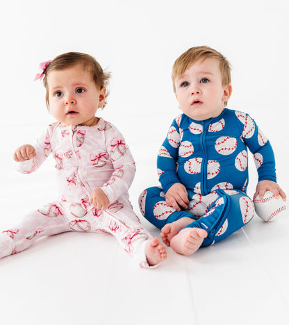 Two babies wearing coordinating bamboo pajamas with baseballs on a white background
