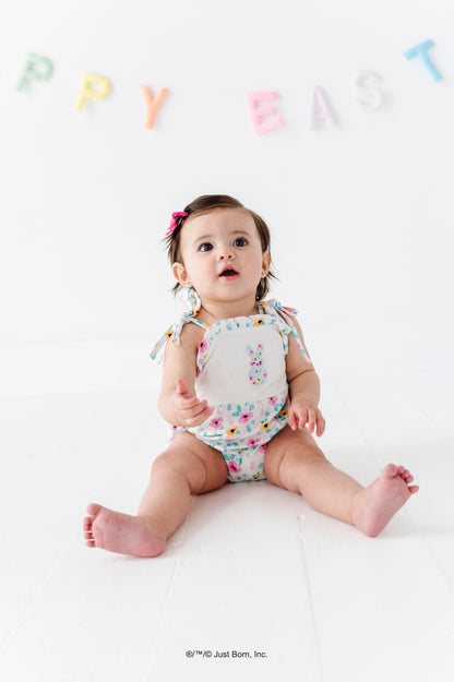 Baby wearing a colorful PEEPS® floral romper with 'Happy Easter' banner in the background