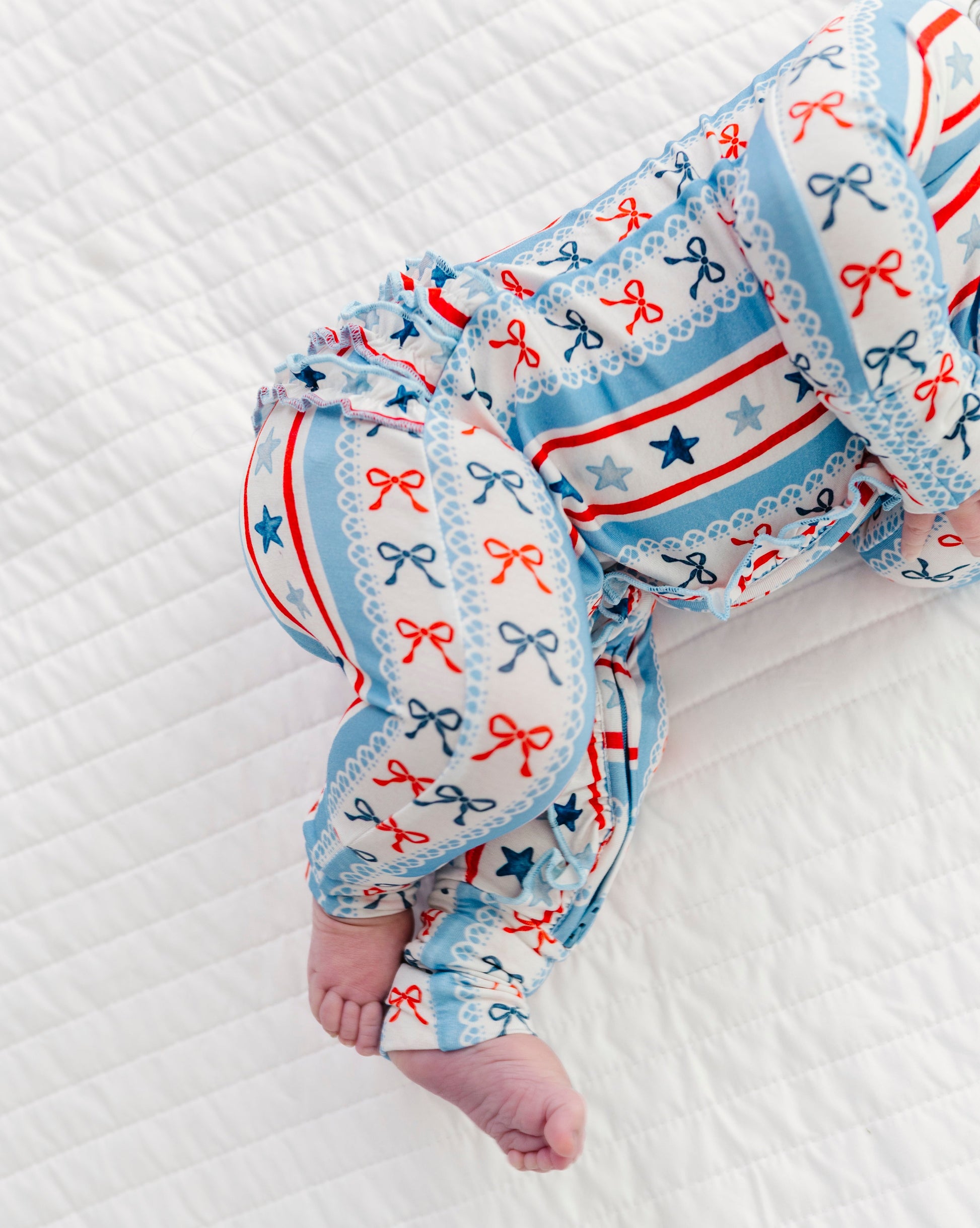Baby wearing a patriotic bamboo convertible romper with star and bow patterns on a white textured surface.