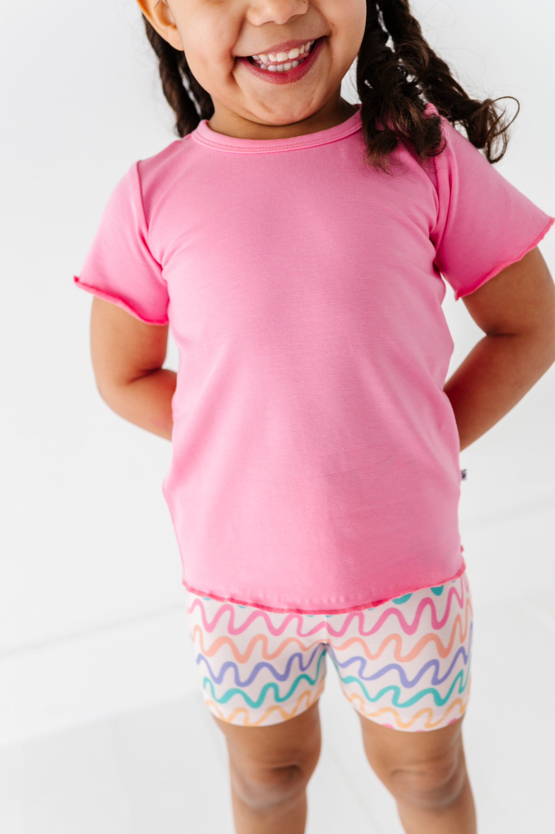 Child wearing a pink shirt and colorful wavy shorts on a white background