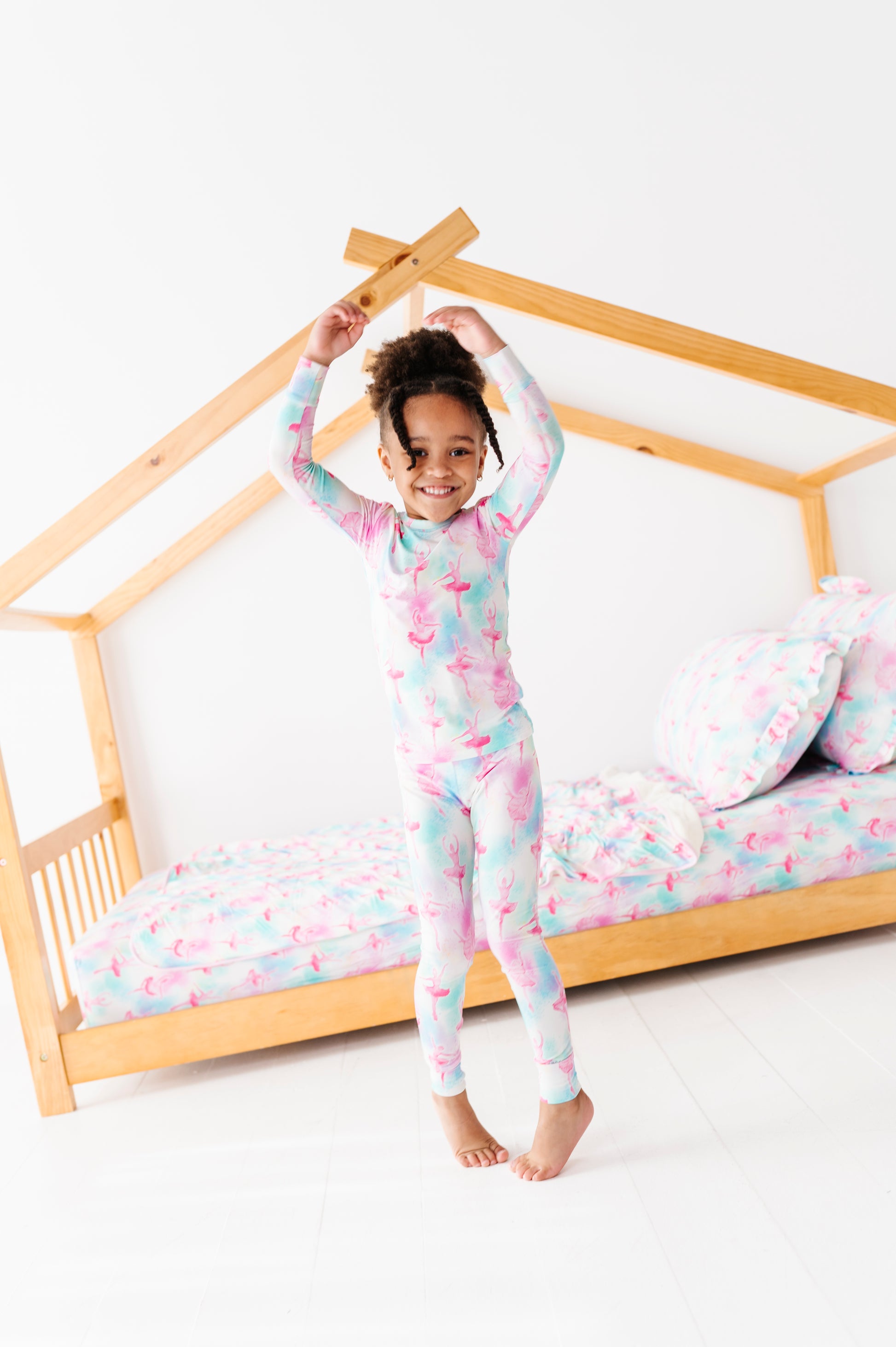 Little girl in bamboo ballerina pajamas twirling in front of matching ballerina bedding on a twin-size bed 