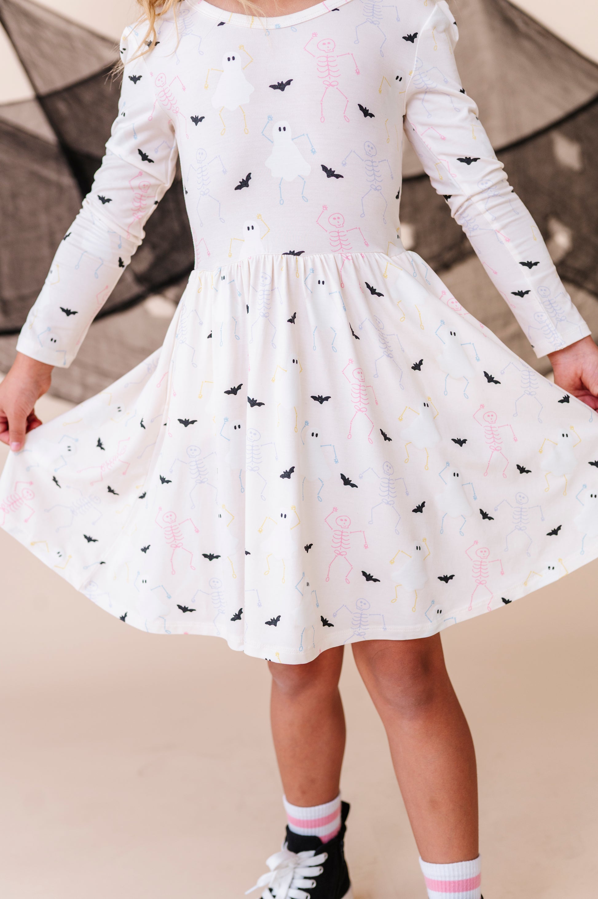 Child wearing a white dress with halloween patterns against a neutral background