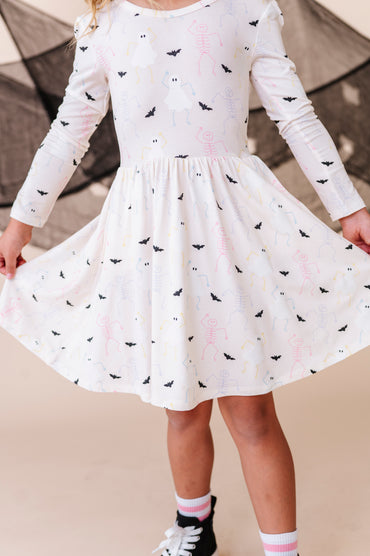 Child wearing a white dress with halloween patterns against a neutral background
