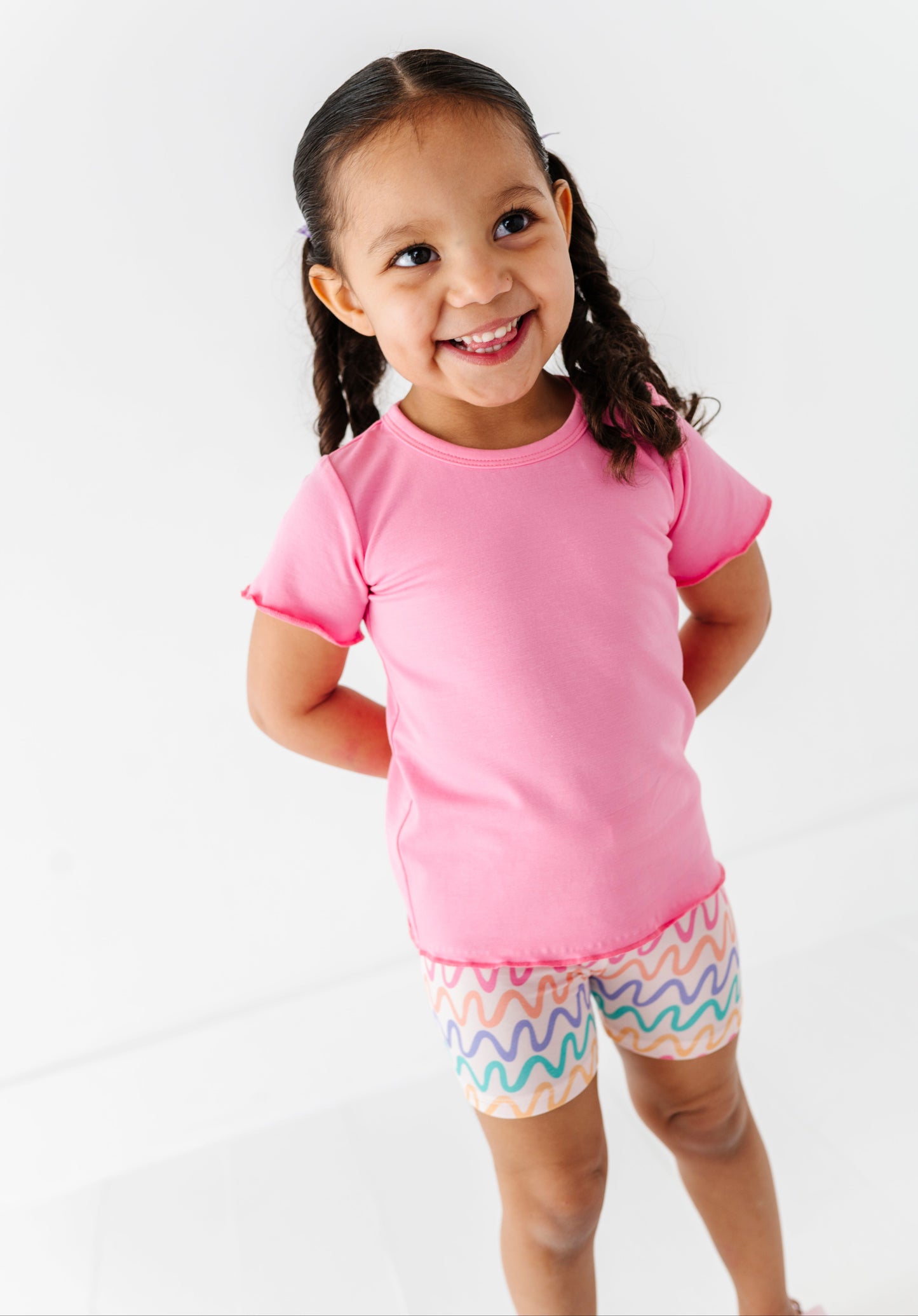 Young girl wearing a pink bamboo/cotton shirt and colorful bamboo biker shorts on a white background