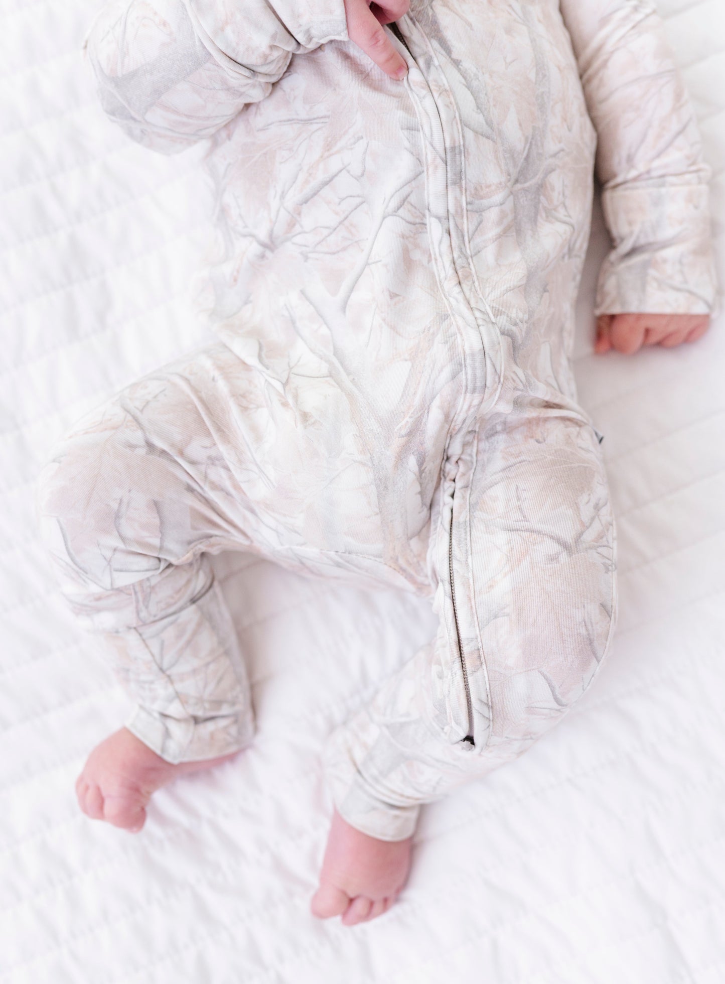 Baby wearing a tree camo romper lying on a white blanket