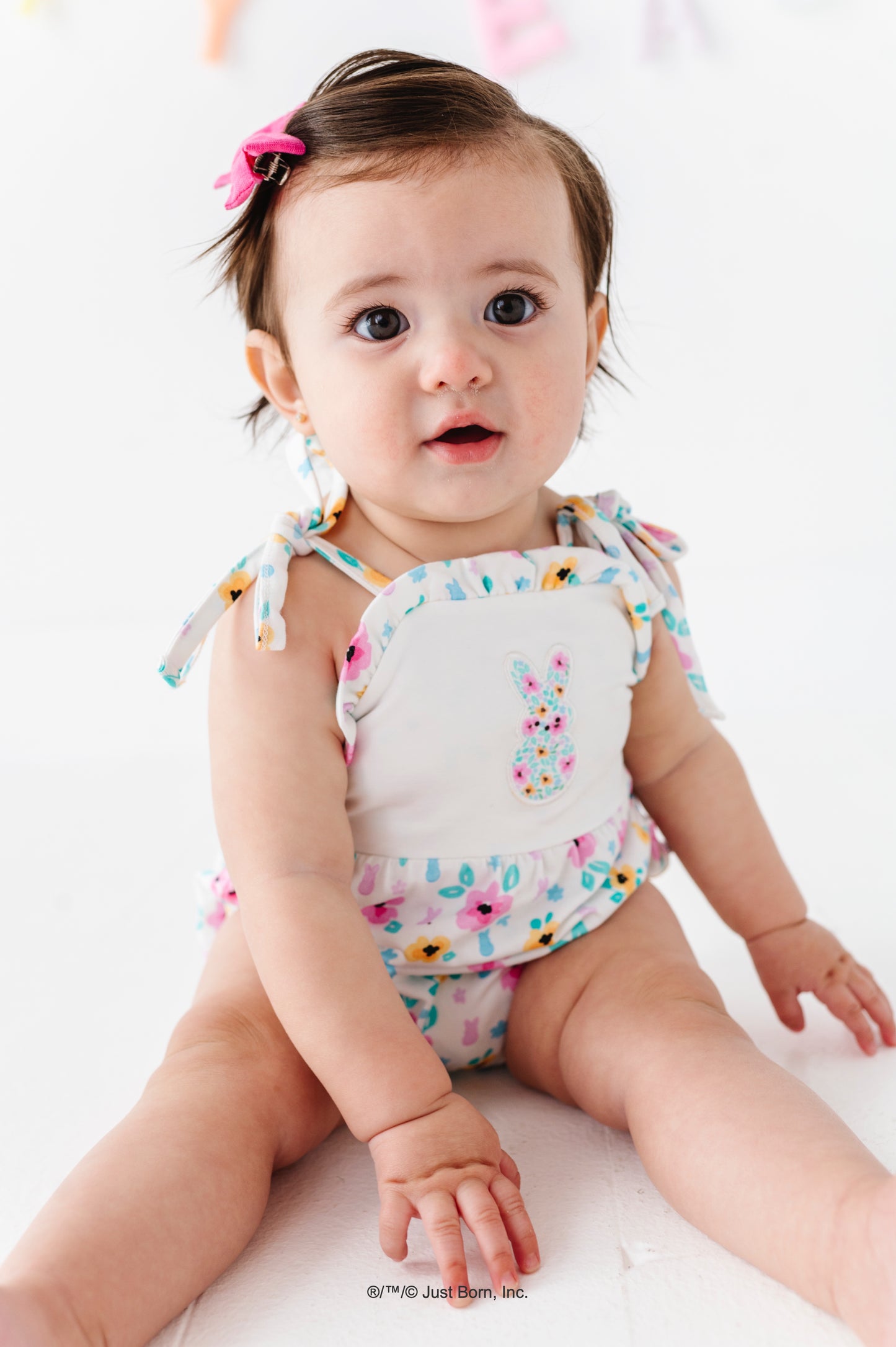 Baby wearing a floral PEEPS® bubble romper sitting on a white surface