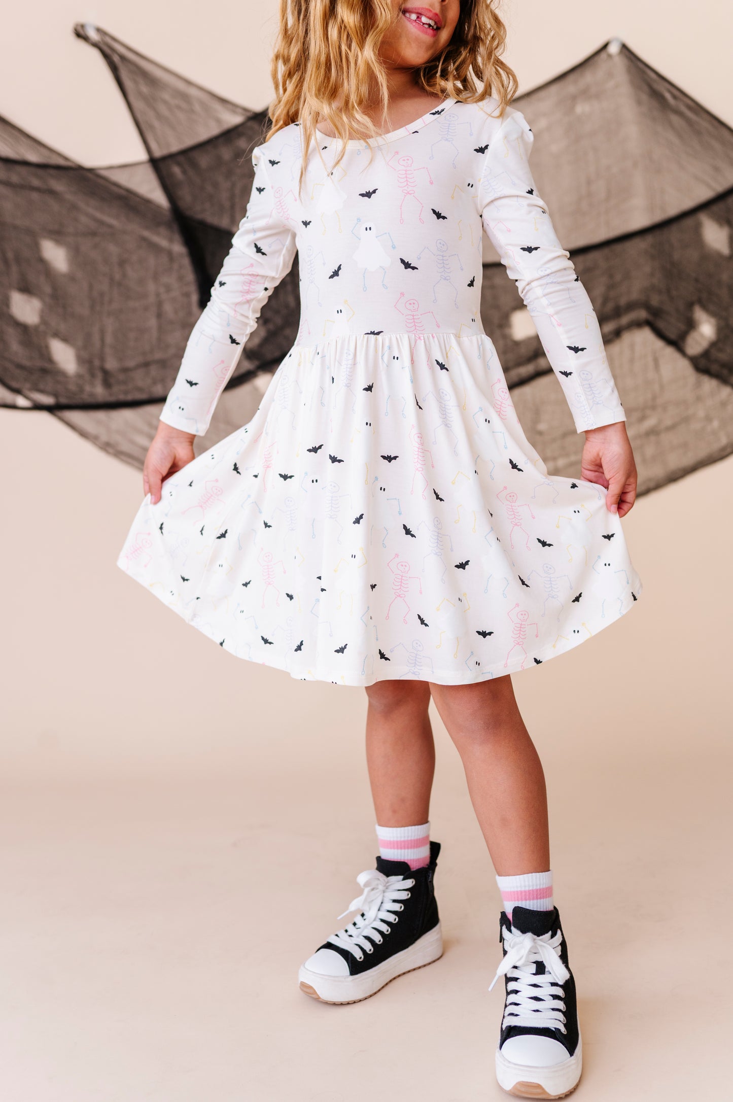 Child wearing a white dress with ghost patterns and black high-top sneakers on a beige background