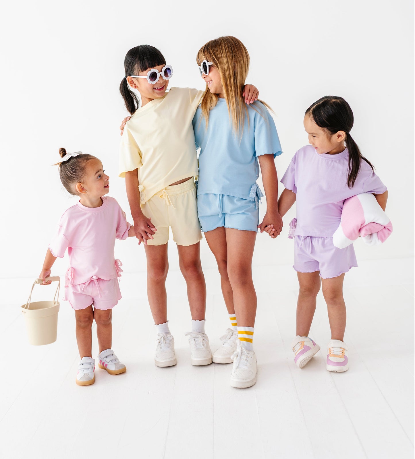 Four children in pastel outfits standing together on a white background