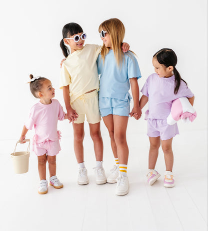 Four children in pastel outfits standing together on a white background