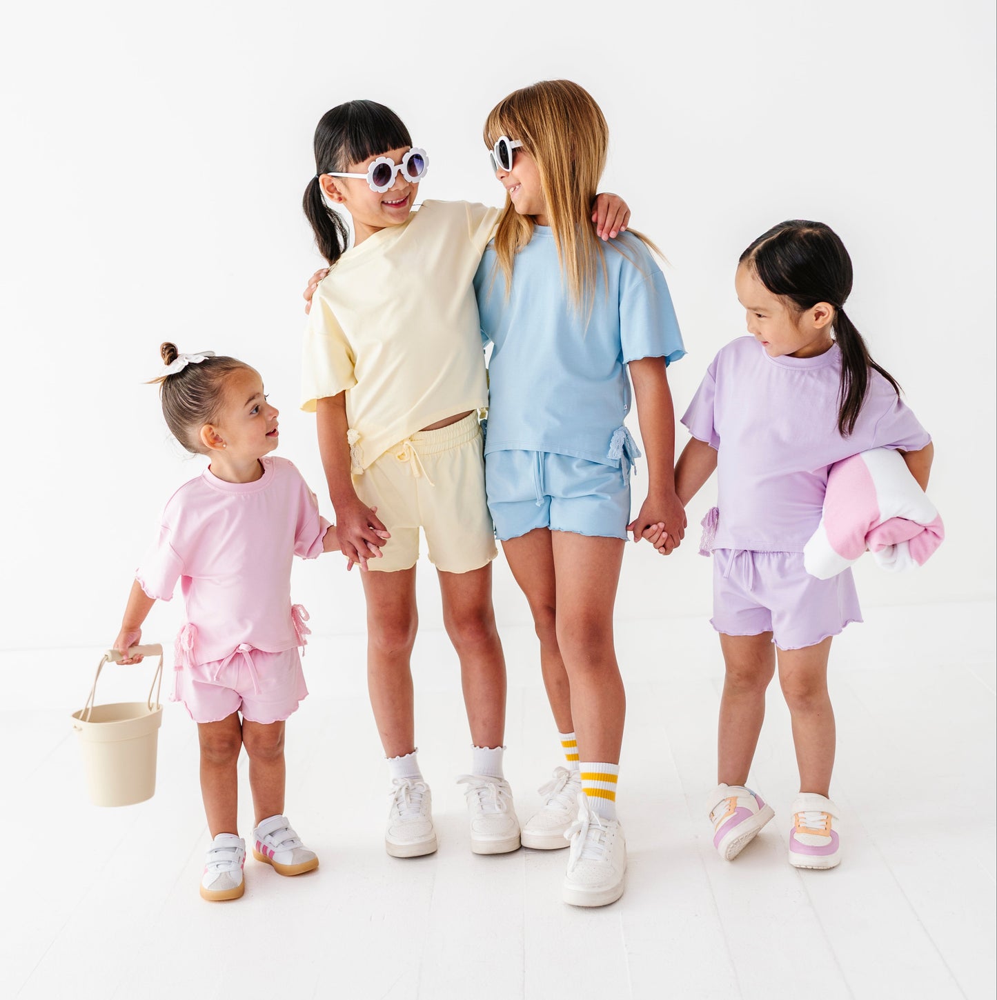 Four children in pastel outfits standing together on a white background