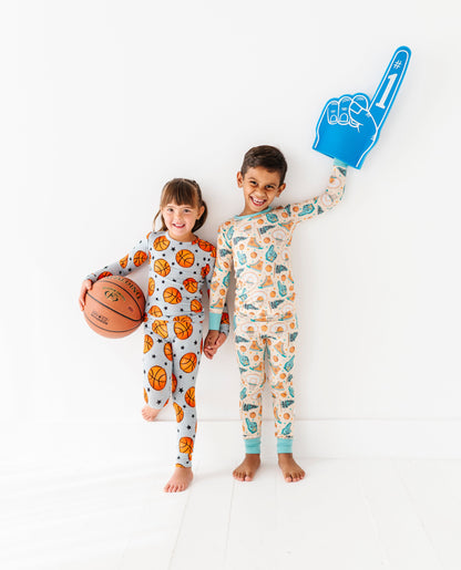 Two children in basketball bamboo pajamas holding a basketball and foam hand on a white background