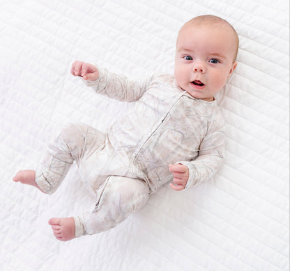 Baby lying on a white textured blanket wearing a light gray tree camo  romper .