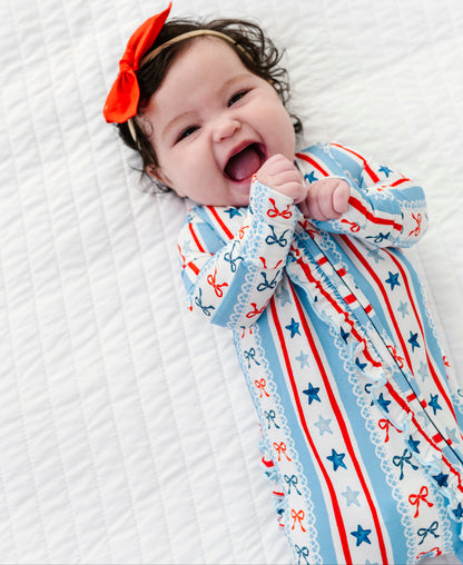 Baby wearing patriotic bamboo sleepwear with bows and stars, lying on a white textured surface.