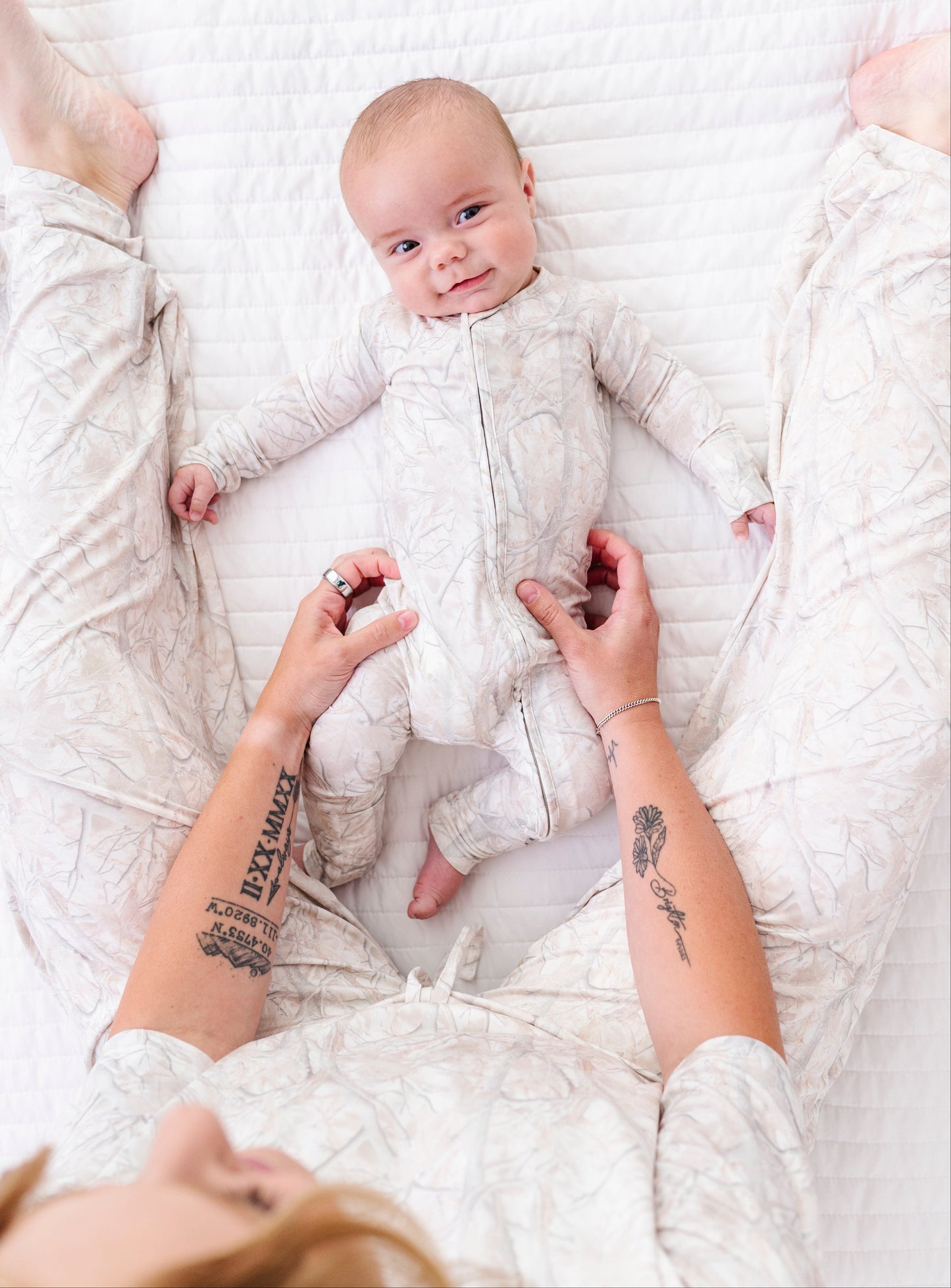 Baby lying on a white blanket with a person's hands holding the baby