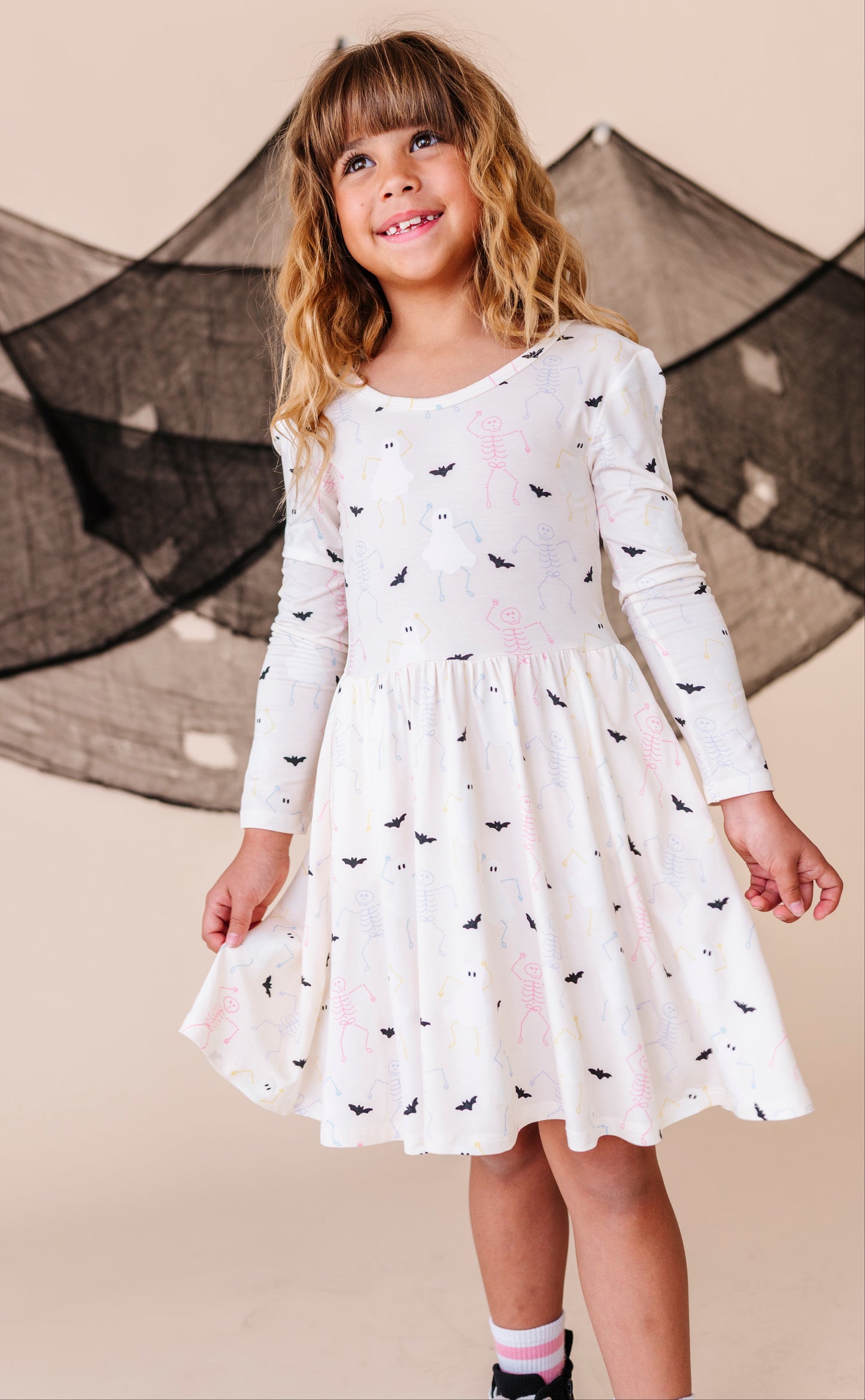 Young girl wearing a white dress with spooky patterns in front of a decorative net.
