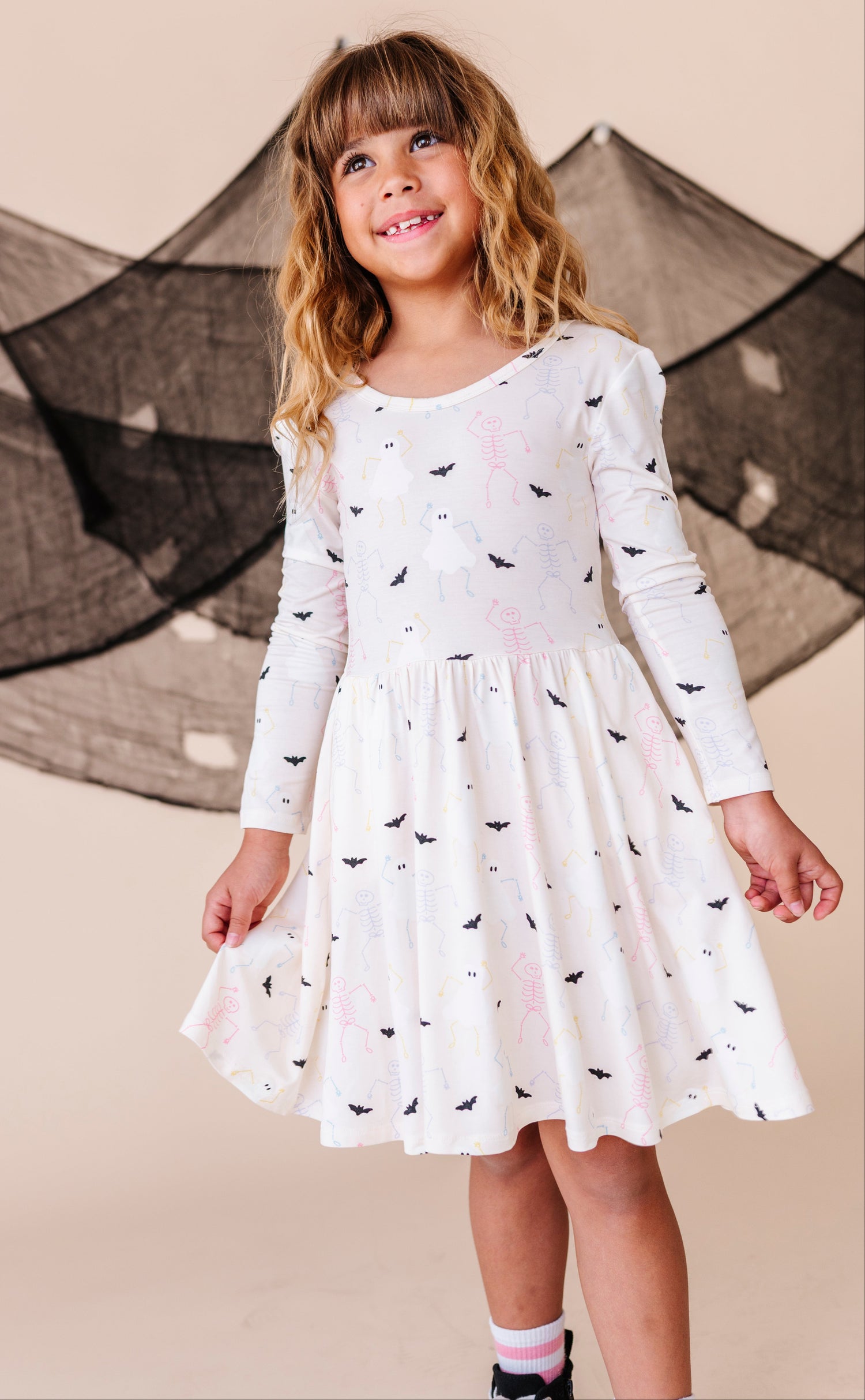 Young girl wearing a white dress with spooky patterns in front of a decorative net.