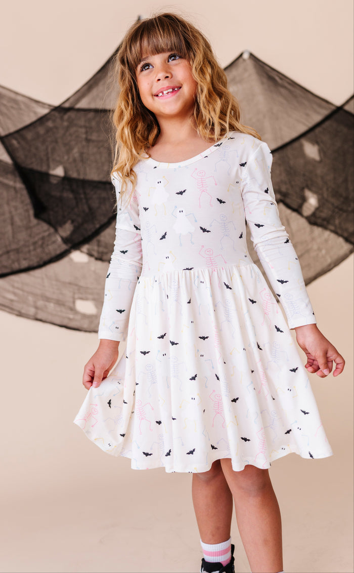 Young girl wearing a white dress with spooky patterns in front of a decorative net.