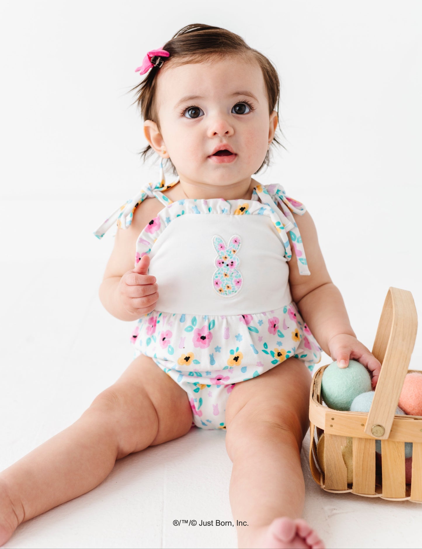 Baby in a floral PEEPS® outfit with Easter basket with Easter eggs on a white background