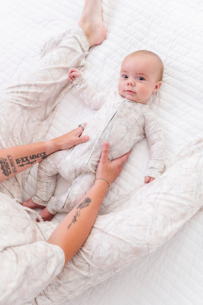 Baby lying on a white textured surface with a person's hand holding the baby's foot.