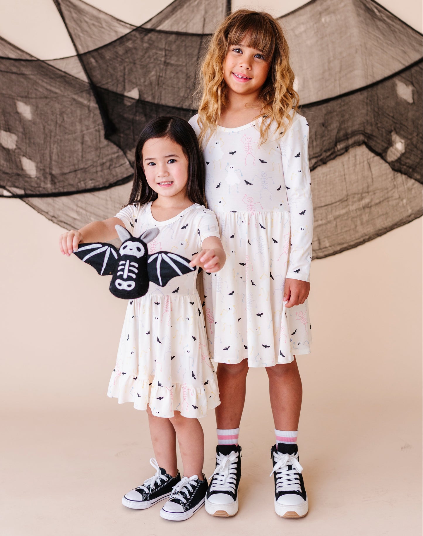 Two young girls in cream colored halloween dresses standing in front of a decorative net.