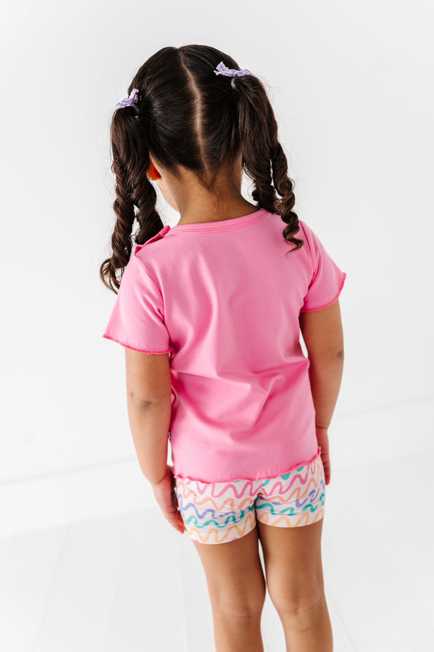Child wearing a pink bamboo/cotton shirt and patterned bamboo biker shorts on a white background