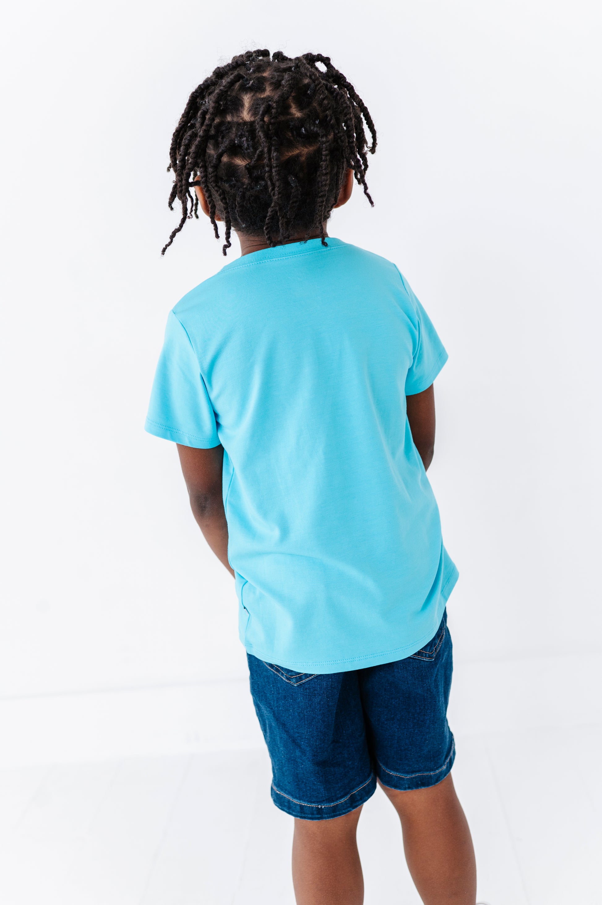Little boy wearing a light blue bamboo t-shirt and denim shorts on a white background