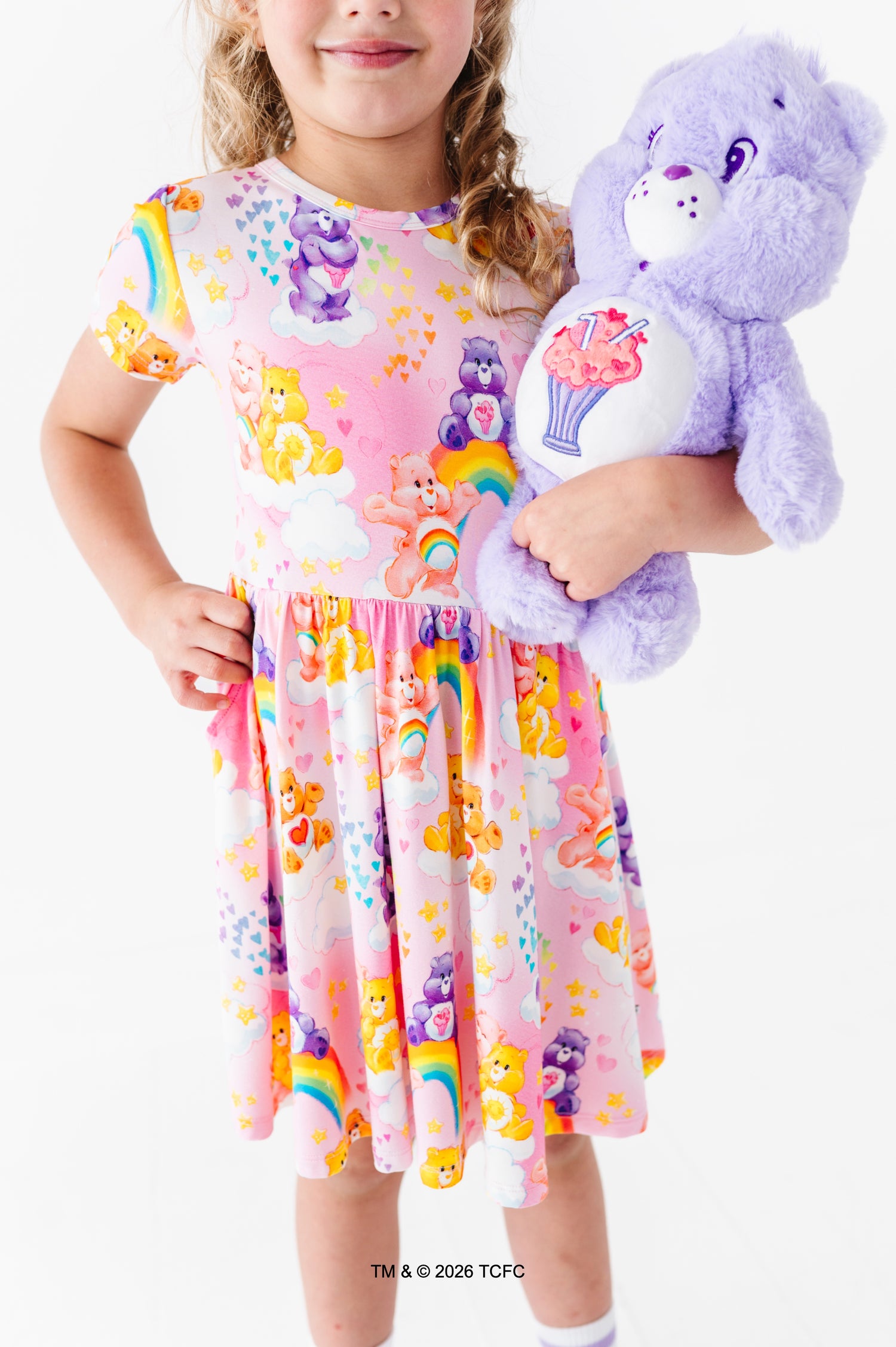 Child wearing a colorful Care Bears™ dress, holding a purple Care Bears™ plush 