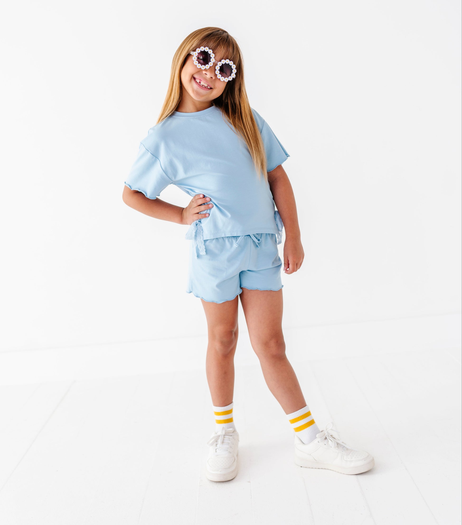 Young girl wearing a light blue outfit with white sneakers on a white background