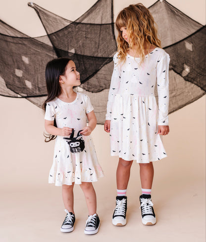 Two young girls wearing cream colored Halloween  dresses with black patterns standing in front of a decorative net.