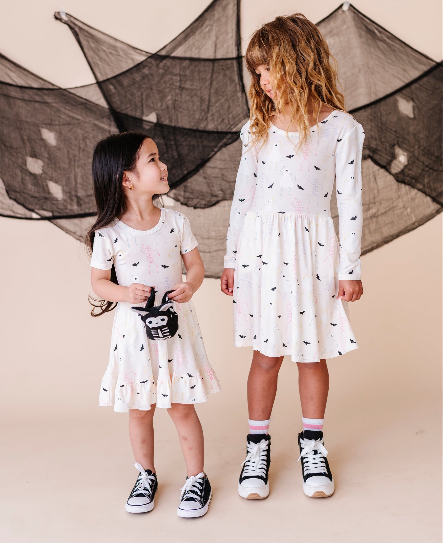 Two young girls wearing white dresses with halloween patterns standing in front of a decorative net.
