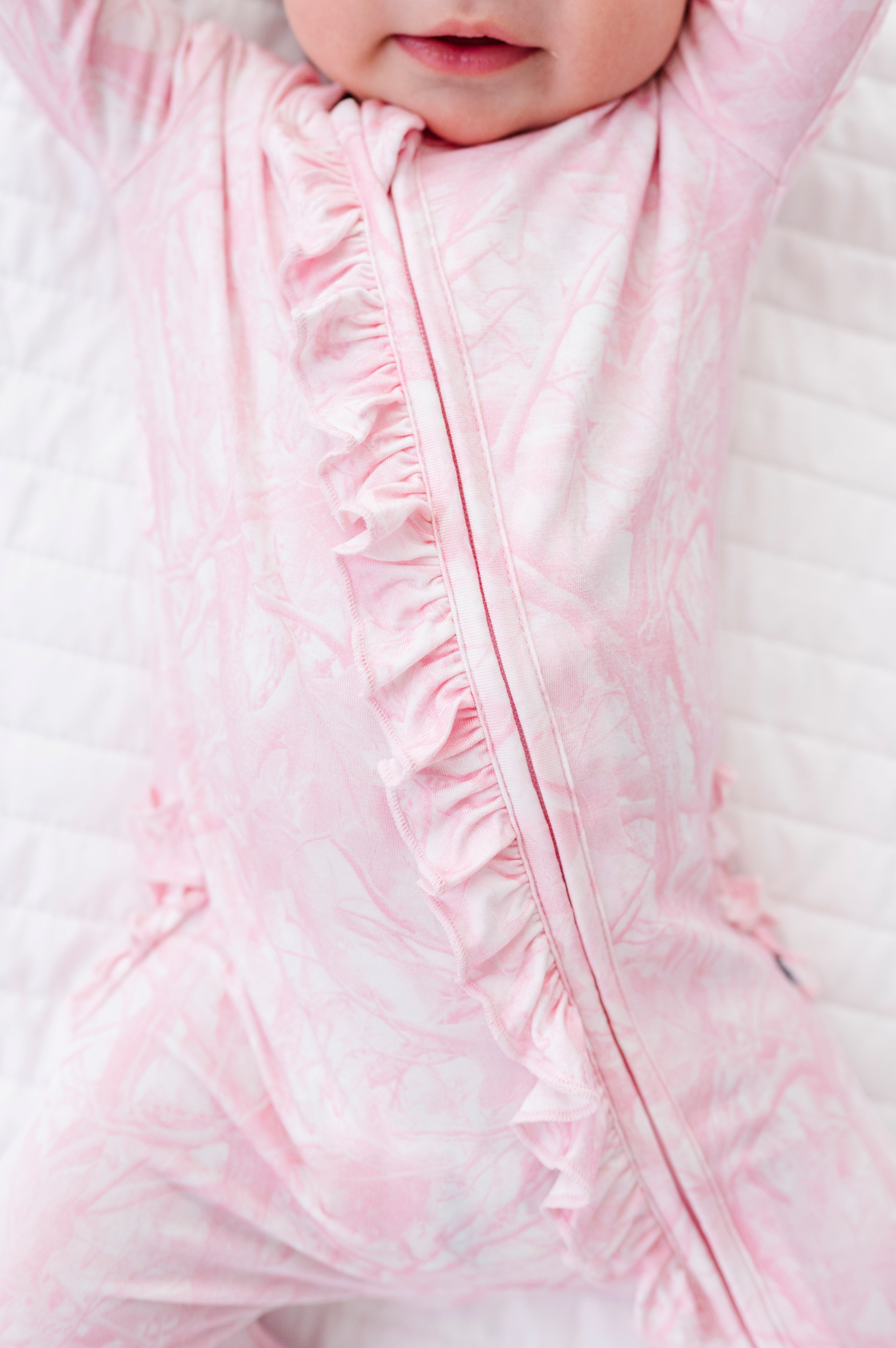 Close-up of a baby in a pink tree camo romper with ruffled details.