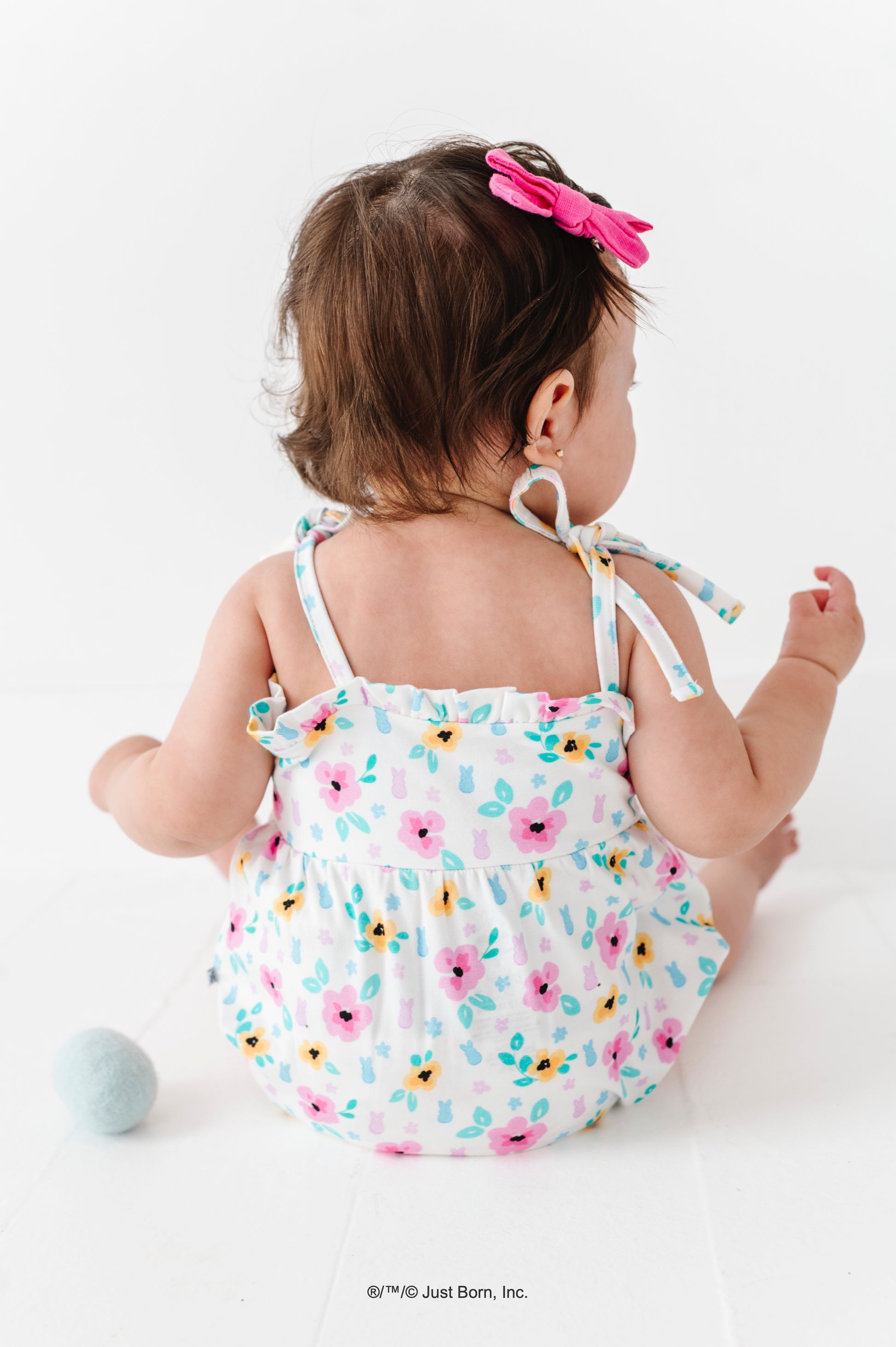 Baby wearing a floral PEEPS® romper and pink bow on a white background 