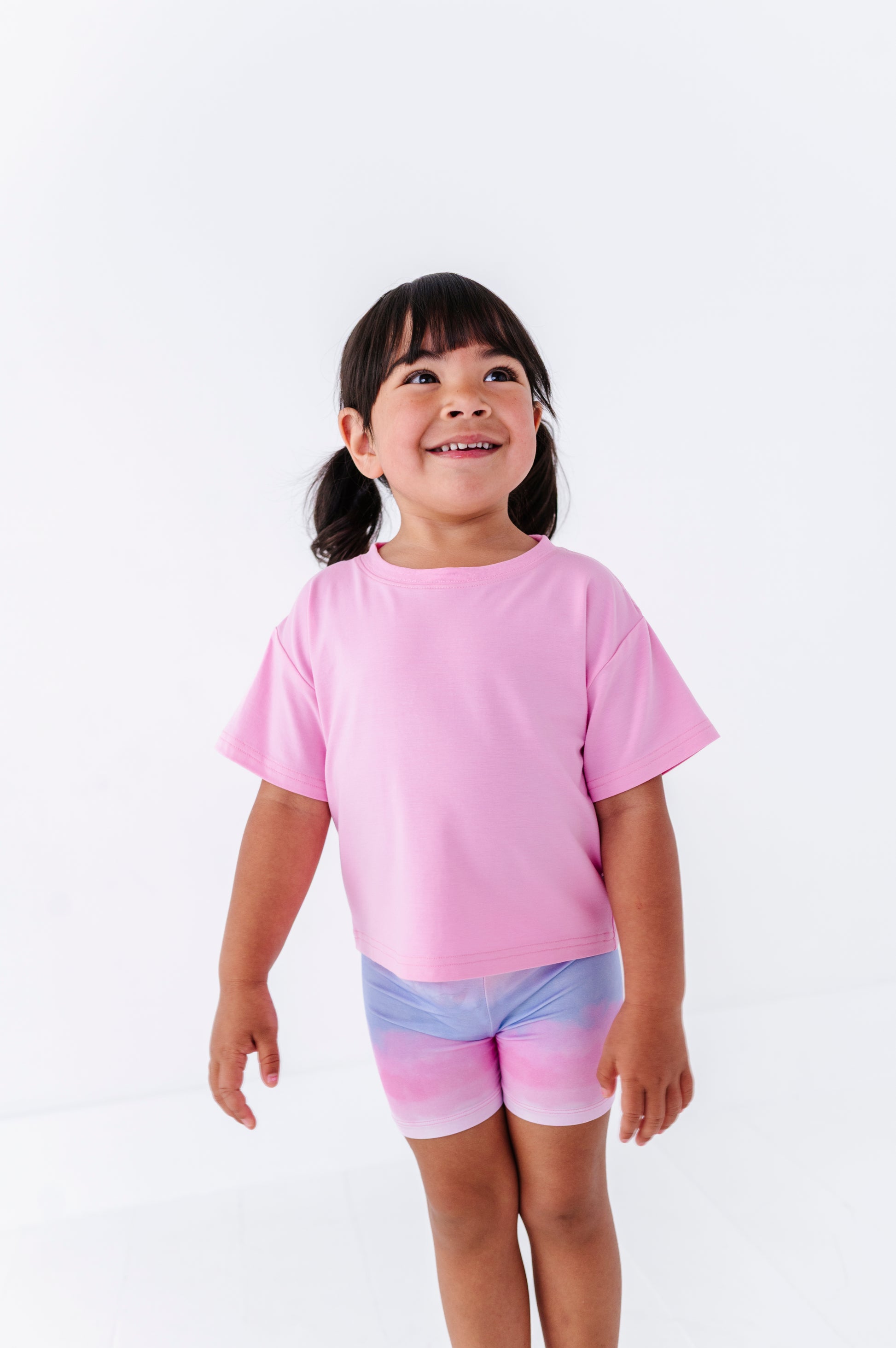 Child wearing a pink shirt and colorful bamboo biker shorts on a white background