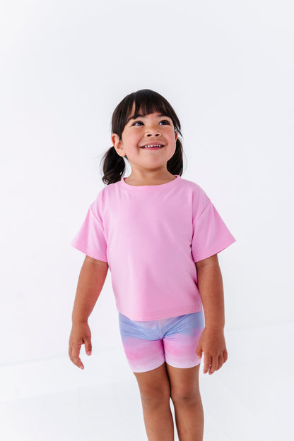 Child wearing a pink shirt and colorful bamboo biker shorts on a white background