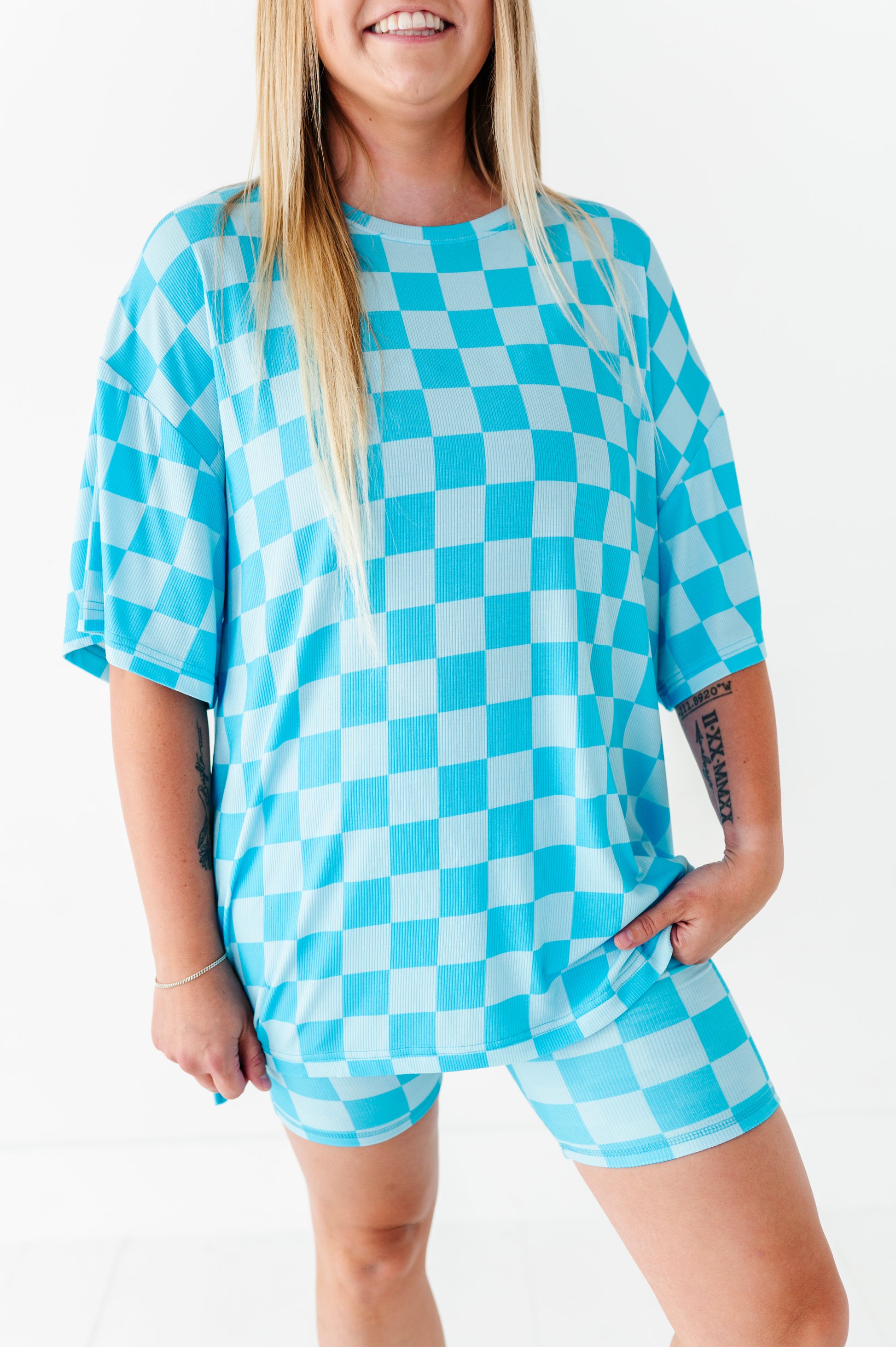 A woman wearing an oversized short-sleeve t-shirt and matching shorts in a bright blue and white checkerboard pattern, photographed against a clean white background.