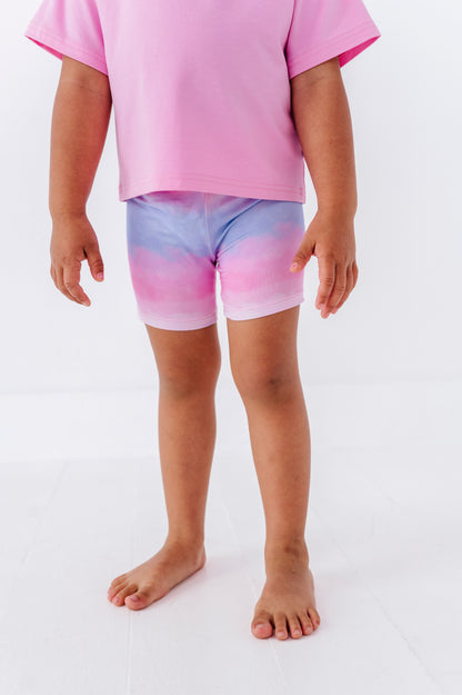Child wearing pink and purple tie-dye shorts on a white background